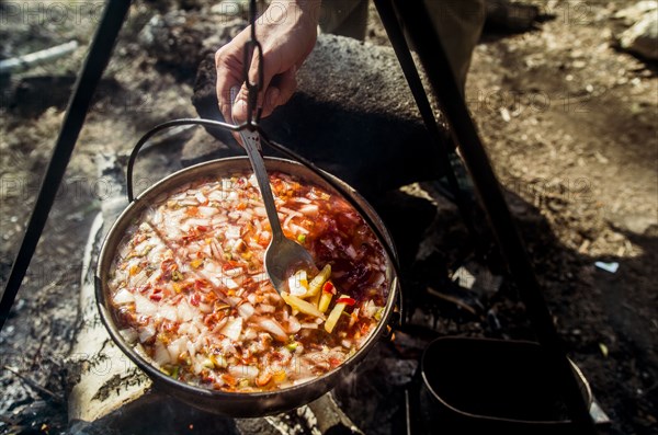 Close up of person stirring soup cooking over campfire