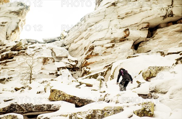 Caucasian hiker climbing snowy rock formations