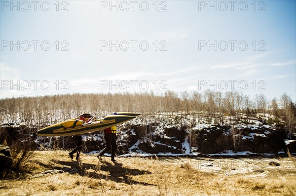 Caucasian couple carrying catamaran in snowy field