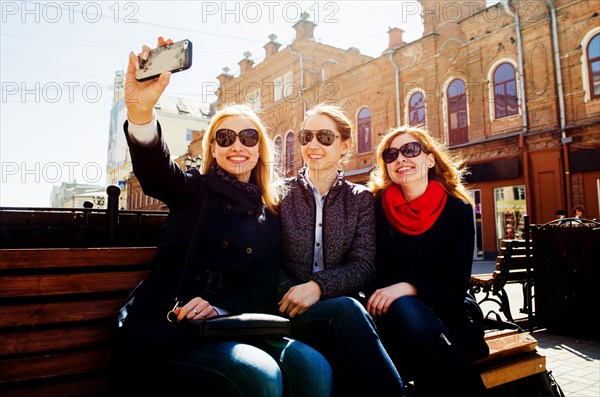 Caucasian women taking cell phone photographs on city bench