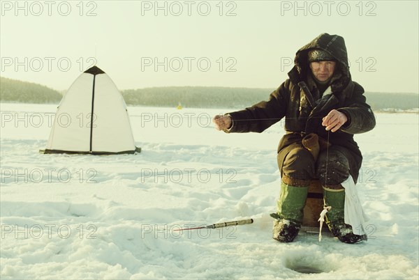 Caucasian man ice fishing on remote lake