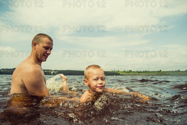 Caucasian father and son swimming in lake