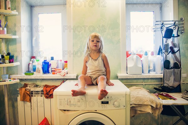 Caucasian girl sitting on washing machine