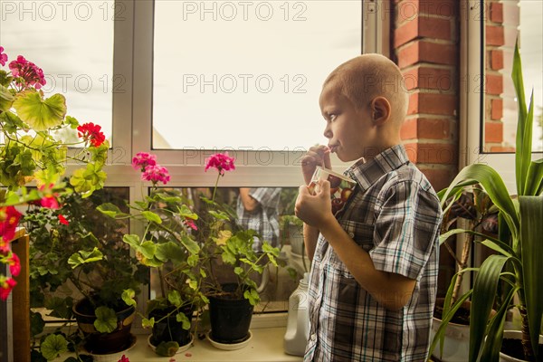 Caucasian boy drinking juice from mug by window