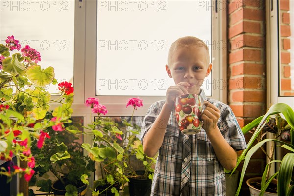 Caucasian boy drinking juice from mug by window