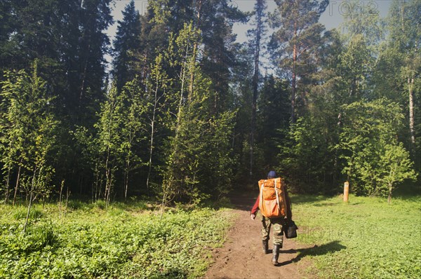 Caucasian backpacker hiking on dirt path in forest