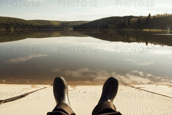 Boots of person resting on dock at lake