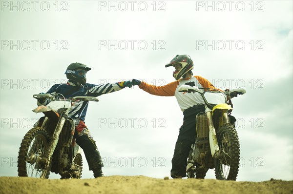 Caucasian men bumping fists on dirt bikes