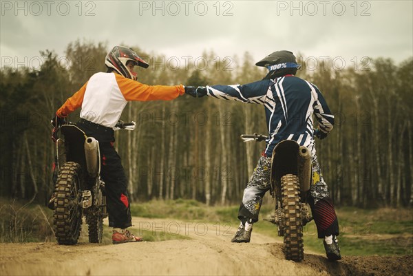 Caucasian men bumping fists on dirt bikes