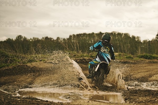 Caucasian man riding dirt bike in puddle