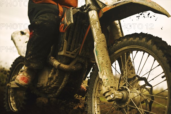 Close up of man riding muddy dirt bike