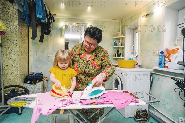 Caucasian grandmother and granddaughter ironing laundry