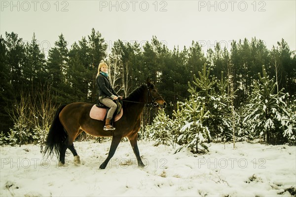 Caucasian woman riding horse on snowy path