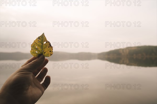 Hand holding autumn leaf at remote lake