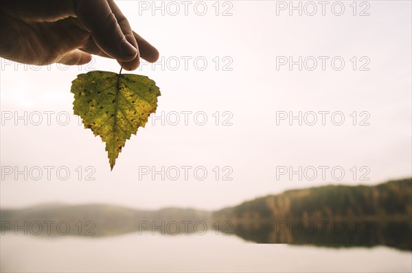 Hand holding autumn leaf at remote lake