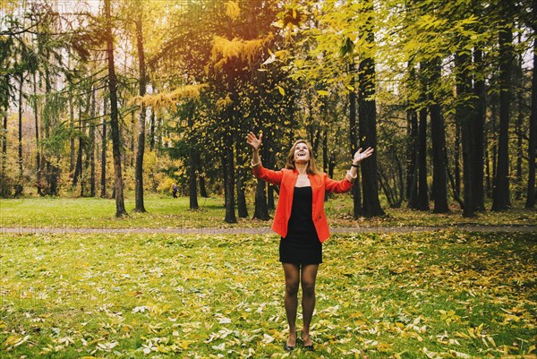 Caucasian woman tossing autumn leaves in park