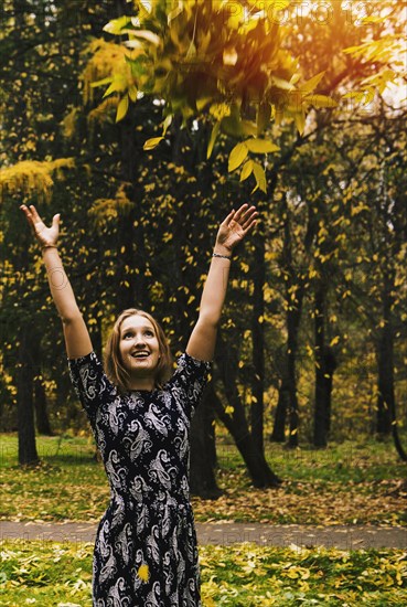 Caucasian woman tossing autumn leaves in park