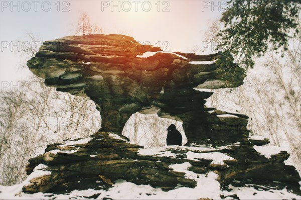 Hiker sitting under rock formation in snow