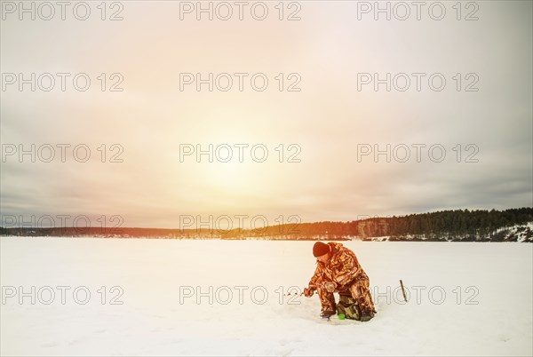 Man ice fishing in frozen lake