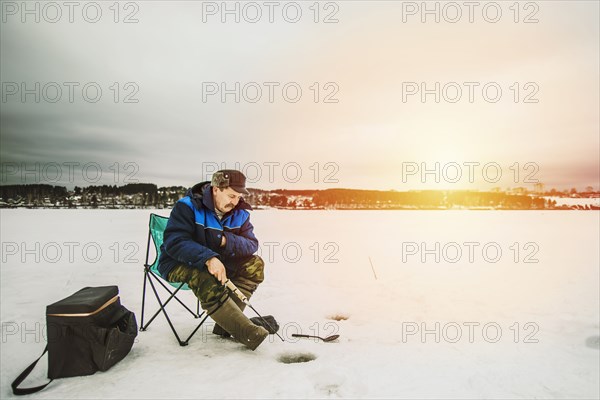 Man ice fishing in frozen lake