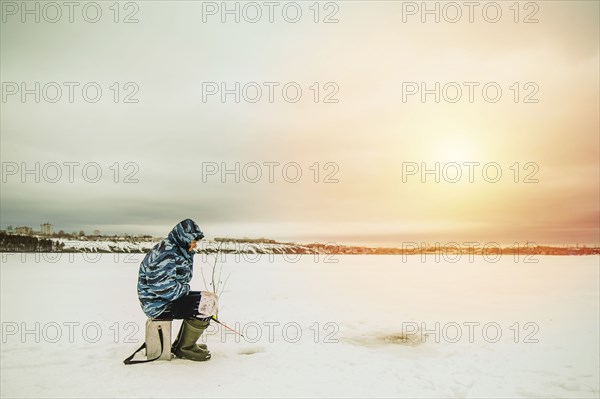 Man ice fishing in frozen lake