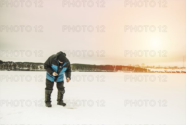 Man ice fishing in frozen lake