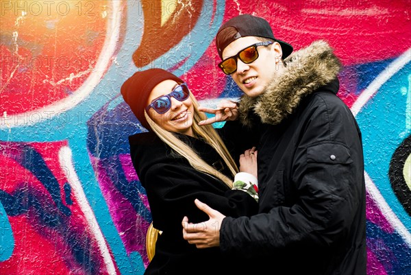 Couple gesturing peace at graffiti wall