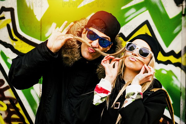 Couple making mustache with hair of woman at graffiti wall