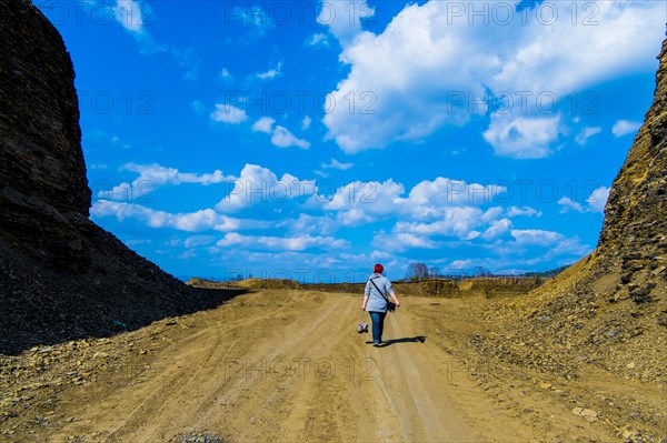 Distant woman walking on dirt road carrying boots