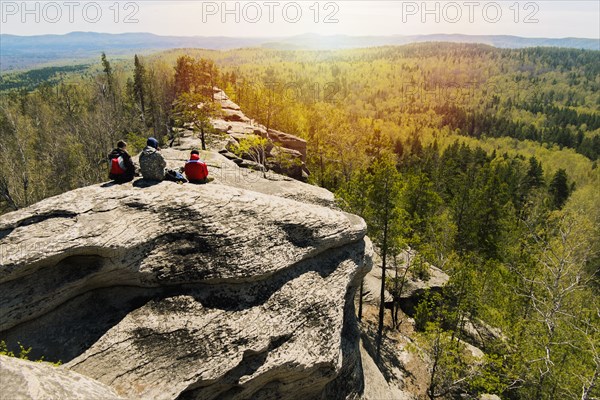 Caucasian friends sitting on mountain rock admiring scenic view