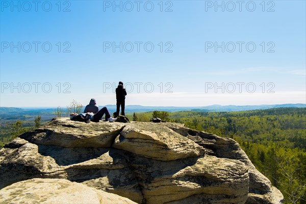 Caucasian friends sitting on mountain rock admiring scenic view