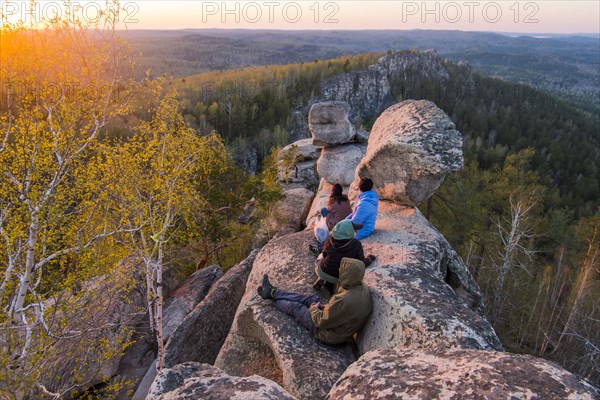 Caucasian friends sitting on mountain rock admiring scenic view