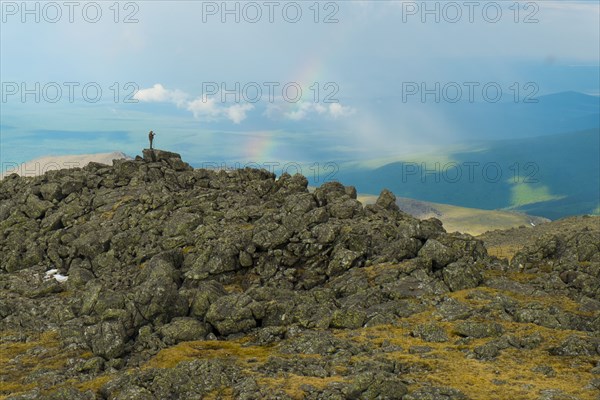 Man standing on rock formation looking at rainbow