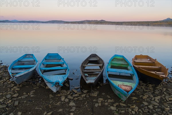 Five empty rowboats on rocky shore of lake at sunset