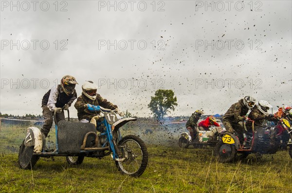Caucasian racers on motorcycles with side cars spraying dirt