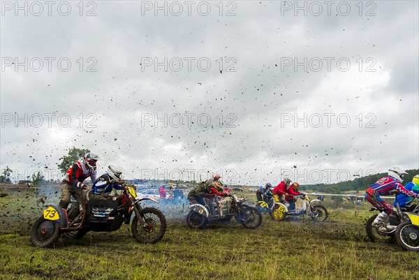 Caucasian racers on motorcycles with side cars spraying dirt