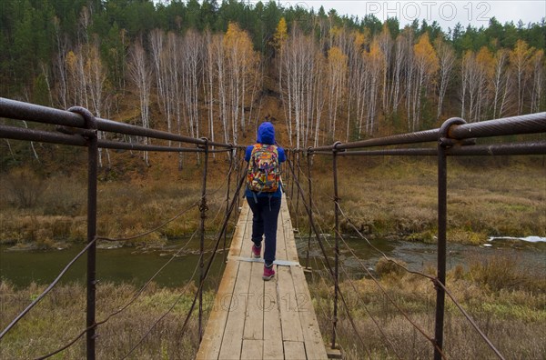 Caucasian woman crossing river on wooden footbridge
