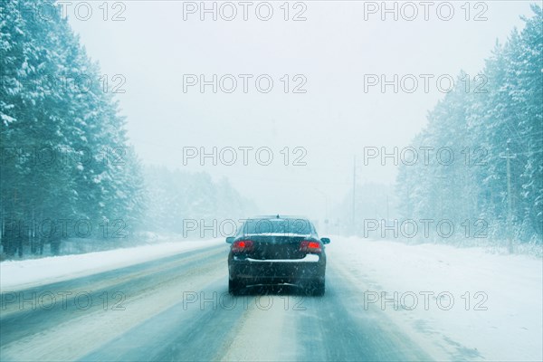 Car driving on tree-lined road in winter