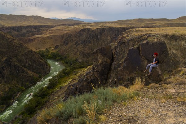 Caucasian woman sitting on mountain rocks photographing river