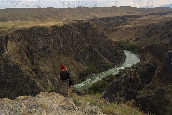 Caucasian woman sitting on mountain rocks photographing river