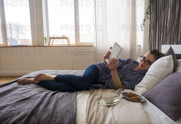 Caucasian woman laying on bed reading digital tablet