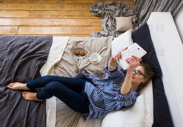 Caucasian woman laying on bed posing for selfie with digital tablet