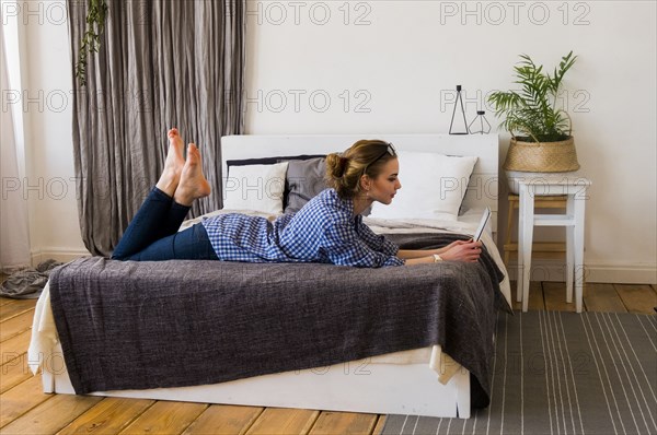 Caucasian woman laying on bed reading digital tablet