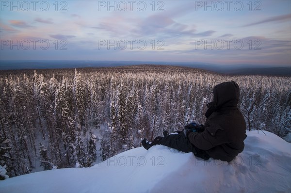 Caucasian man sitting in snow admiring scenic view of forest