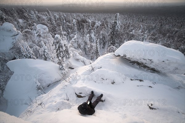 Caucasian man laying in snow texting on cell phone