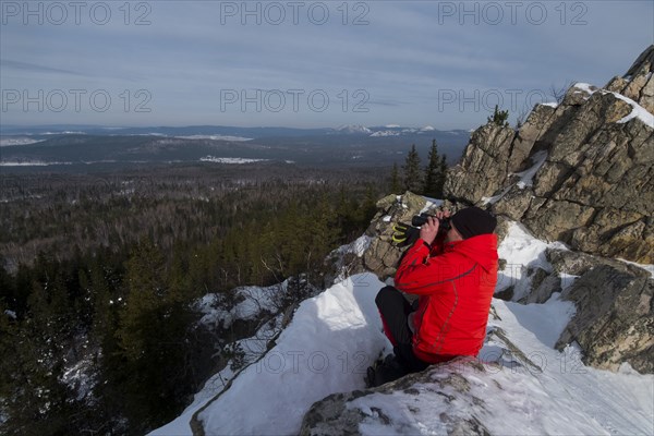 Caucasian man sitting in snow admiring scenic view of forest