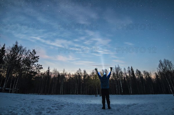 Caucasian man wearing headlamp with arms raised in winter