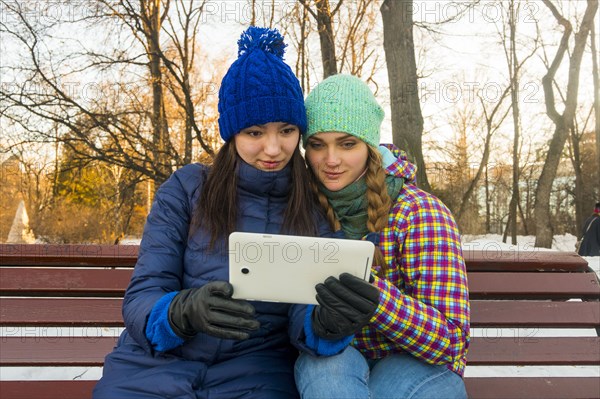 Caucasian women sitting on park bench in the winter holding digital tablet