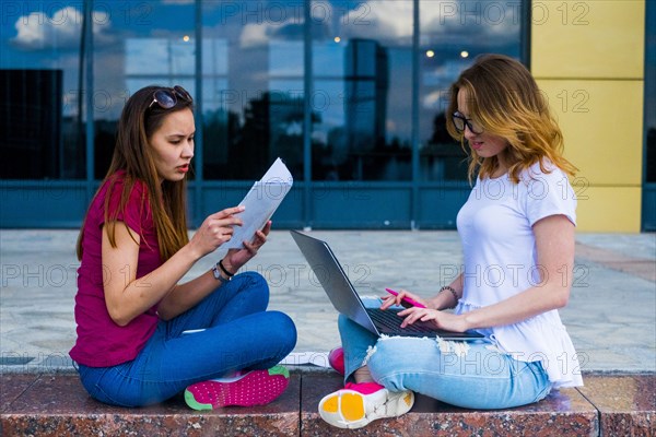 Caucasian women reading paperwork and using laptop outdoors