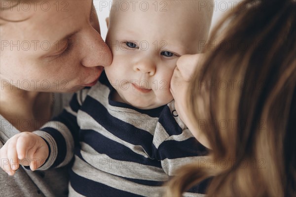 Caucasian mother and father kissing baby son on cheek